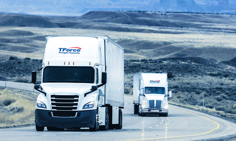 Deux camions de TForce Freight Canada roulant sur l’autoroute devant les prairies canadiennes