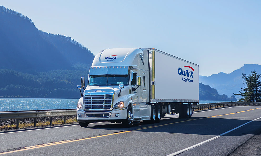 Camion de Quik X Logistics roulant devant un lac canadien