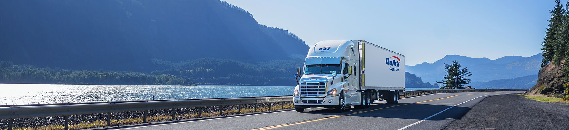 Quik X Logistics truck driving in front of Canadian lake